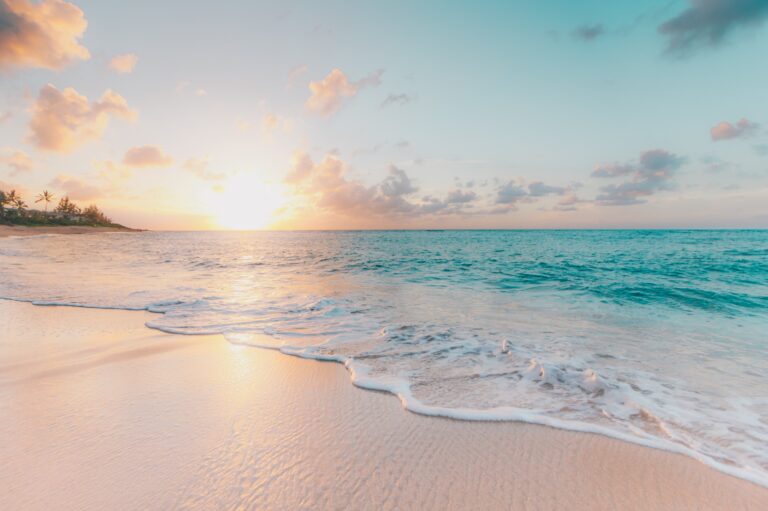 A shoreline featuring a sunrise with aqua and tan hues.